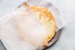 flipping over raw cauliflower pizza crust on a parchment on a pizza pan