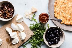 ingredients laid out for cauliflower crust pizza, mozzarella, parmesan, mushrooms, olives