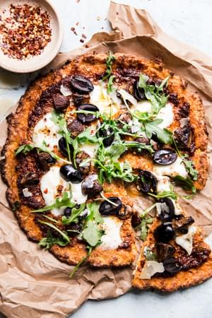 Cauliflower pizza crust pizza with olives, arugula, mozzarella and parmesan cheese