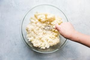 hand smashing cooked cauliflower in a bowl with a fork