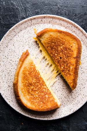 a grilled cheese cut in half made with bread spread with butter and mayo and melted shredded cheddar cheese in the middle
