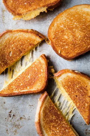 perfectly golden grilled cheese sandwiches cut in half with melted cheese pulling apart in the middle