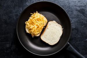 a grilled cheese sandwich cooking in a skillet made with bread spread with butter and mayo and shredded cheddar cheese