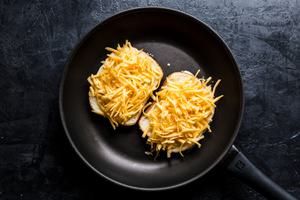 a grilled cheese sandwich cooking in a skillet made with bread spread with butter and mayo and shredded cheddar cheese