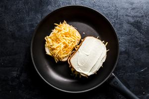 a grilled cheese sandwich cooking in a skillet made with bread spread with butter and mayo and shredded cheddar cheese