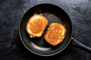 a grilled cheese sandwich cooking in a skillet made with bread spread with butter and mayo and shredded cheddar cheese