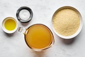 Dried couscous, chicken stock, olive oil and salt in prep bowls to make perfect couscous at home