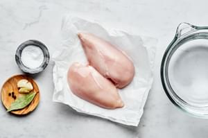 raw chicken breast, water, salt, peppercorns, bay leaf and a garlic clove in bowls to make perfect poached chicken