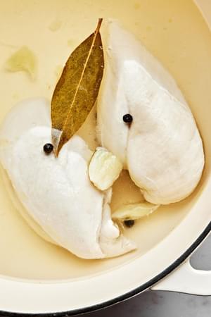chicken breasts being poached in water, salt, peppercorn, garlic and a bay leaf