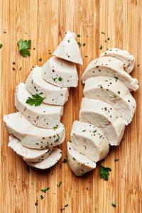 perfect poached chicken sliced on a cutting board cooked in chicken broth, salt, bay leaf, peppercorns and garlic