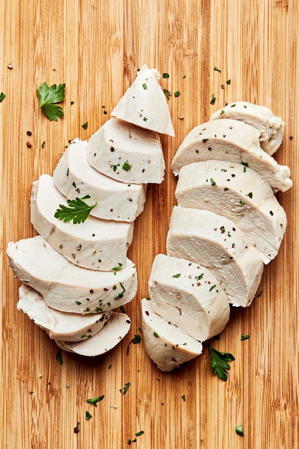 perfect poached chicken sliced on a cutting board cooked in chicken broth, salt, bay leaf, peppercorns and garlic