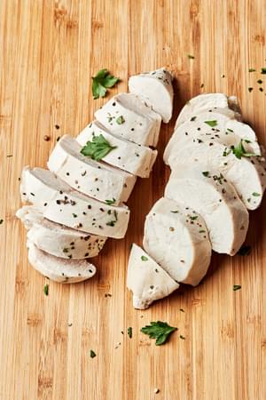 perfect poached chicken sliced on a cutting board cooked in chicken broth, salt, bay leaf, peppercorns and garlic