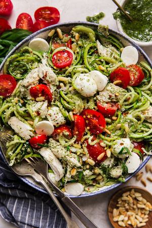 white bowl filled with Pesto chicken zoodle salad topped with fresh cherry tomatoes, pearl mozzarella and toasted pine nuts