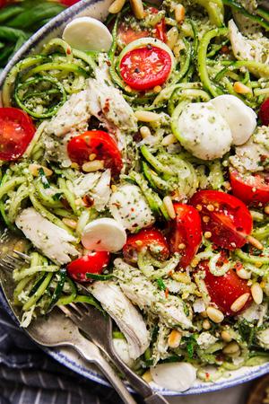 white bowl filled with Pesto chicken zoodle salad topped with fresh cherry tomatoes, pearl mozzarella and toasted pine nuts