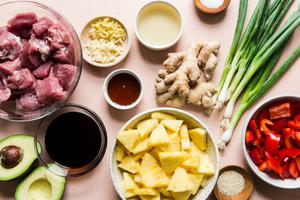 ingredients for pineapple pork stir fry; raw pork, pineapple, red bell peppers, fresh ginger, avocado and green onions