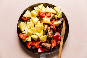 crispy pork bites with raw pineapples and red bell peppers in a skillet