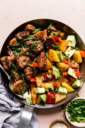 Pineapple Pork Stir Fry with red bell peppers and avocado in a skillet