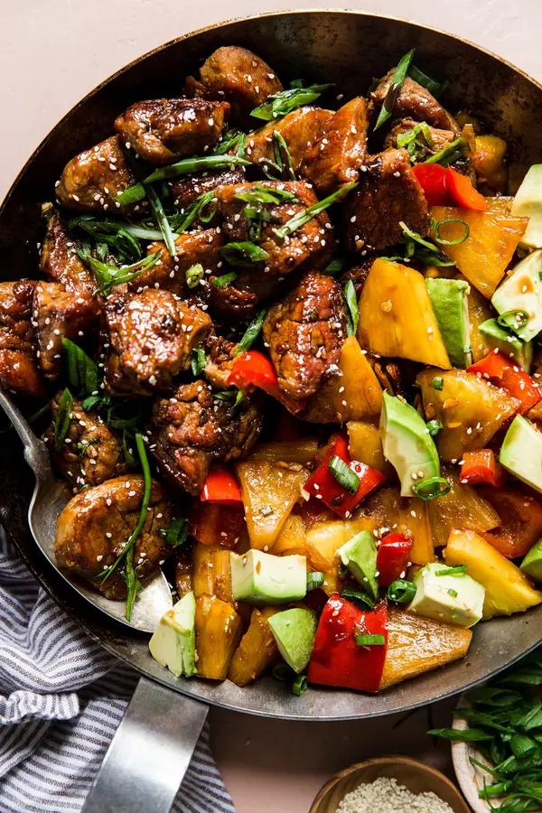 Pineapple Pork Stir Fry with red bell peppers and avocado in a skillet