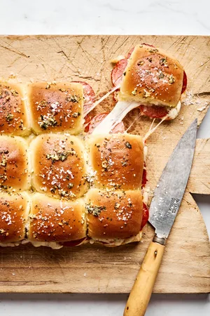pizza sliders on a bread board made with cheese and pepperoni with the tops brushed with butter, garlic, oregano and basil