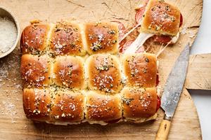 pizza sliders on a bread board made with cheese and pepperoni with the tops brushed with butter, garlic, oregano and basil