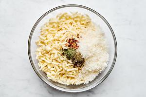 mozzarella, Parmesan, red pepper flakes, oregano, and basil being combined in a bowl