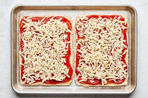 Hawaiian rolls sliced horizontally spread with pizza sauce, mozzarella and Parmesan on a baking sheet