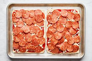 Hawaiian rolls sliced horizontally spread with pizza sauce, mozzarella, Parmesan and pepperoni on a baking sheet