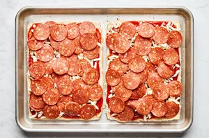 Hawaiian rolls sliced horizontally spread with pizza sauce, mozzarella, Parmesan and pepperoni on a baking sheet