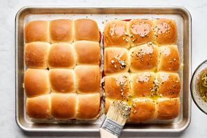 pizza sliders made with Hawaiian rolls being brushed with melted butter and spices