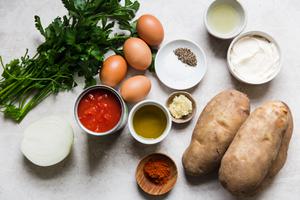 ingredients for patatas bravas in prep bowls including potatoes, onions, canned tomatoes, eggs, spices and parsley