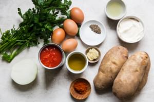 ingredients for patatas bravas in prep bowls including potatoes, onions, canned tomatoes, eggs, spices and parsley