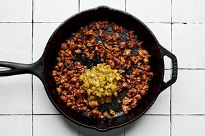 green chilis being added to a skillet with cooked pork chorizo