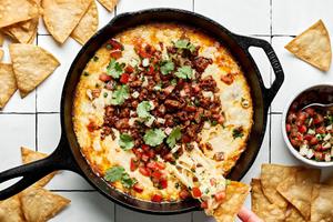 chips being dipped into a skillet of Queso Fundido topped with chorizo, pico de gallo and cilantro