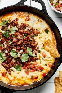 chips being dipped into a skillet of Queso Fundido topped with chorizo, pico de gallo and cilantro
