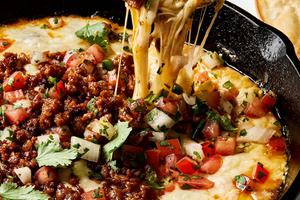 chips being dipped into a skillet of Queso Fundido topped with chorizo, pico de gallo and cilantro