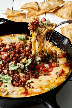 chips being dipped into a skillet of Queso Fundido topped with chorizo, pico de gallo and cilantro