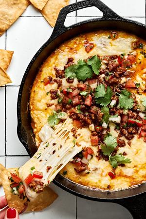 chips being dipped into a skillet of Queso Fundido topped with chorizo, pico de gallo and cilantro