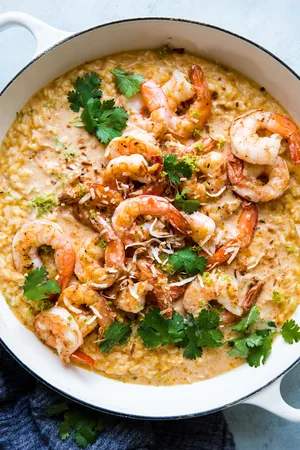 red curry risotto in a white skillet topped with crispy whole shrimp, fresh cilantro and toasted coconut