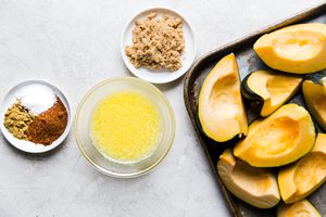 quartered acorn squash on a baking sheet next to cumin, chili powder, salt, melted butter and brown sugar
