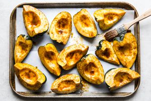 acorn squash quarters on a baking sheet brushed with melted butter, brown sugar, chili powder, cumin and salt, ready to roast