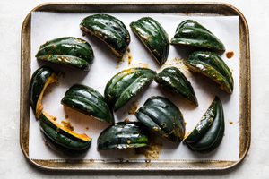 raw quartered acorn squash on a baking sheet skin side up basted with melted butter, brown sugar and spices ready to be baked