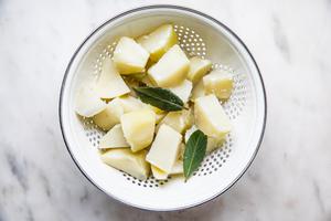 chopped boiled potatoes in a colander with 2 bay leaves