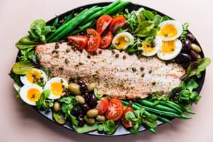Salmon Niçoise Salad on a platter with olives, tomatoes, green beans, fried capers and soft boiled eggs.