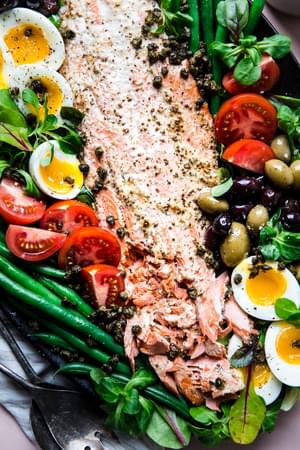 Salmon Niçoise Salad on a platter with olives, tomatoes, green beans, fried capers and soft boiled eggs.