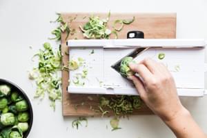 hand shaving Brussels sprouts on a mandolin