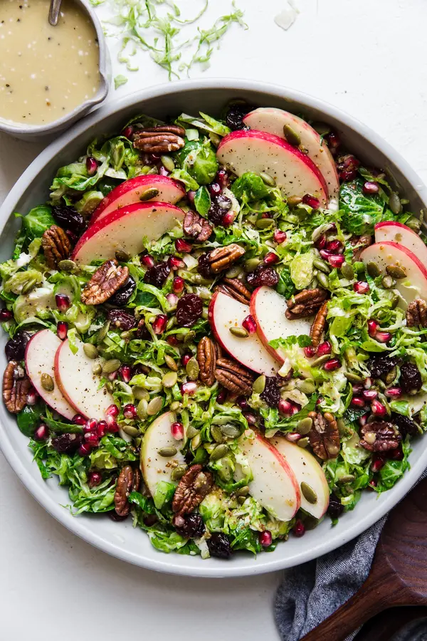 shaved brussels sprout salad in a large bowl topped with apples, pecans, cherries, pumpkin seeds and pecans