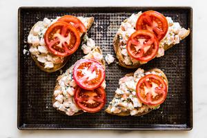 thick slices of crusty bread topped with shrimp mixture and tomato slices on a baking sheet