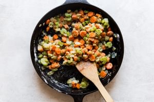 butter, carrots, onion and celery sautéed in a cast iron skillet with flour and seasoning and a wooden spoon.
