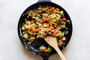 butter, carrots, onion and celery sautéed in a cast iron skillet with flour and seasoning and a wooden spoon.