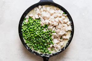 chicken and frozen peas being added a homemade chicken pot pie in a cast iron skillet